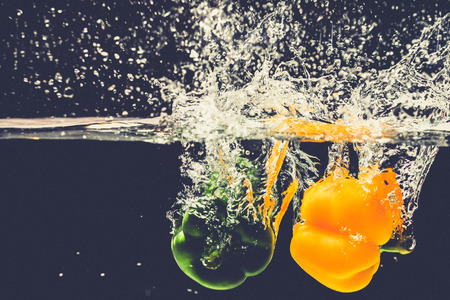 Green yellow bell peppers drop into the water with splash.の写真素材