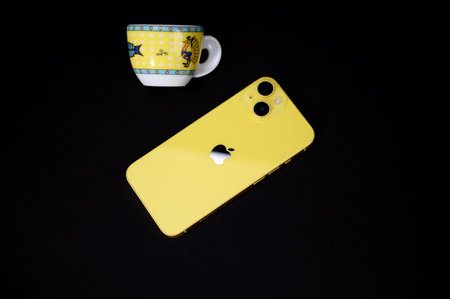Yellow smartphone with a cup on a black background. Close-up.