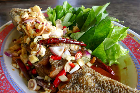 deep fried fish topped with sliced lemongrass and spicy sauce eat with betel leaf - thai food
