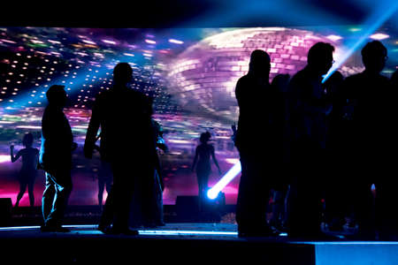 Silhouettes of people celebrate dancing over colourful led screen background