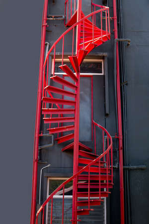 Red metal spiral staircase beside the dark black wallの写真素材