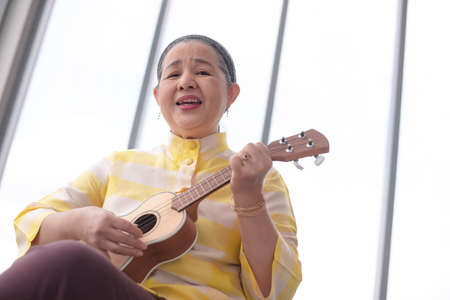 asian grandma playing ukulele with smile in living room