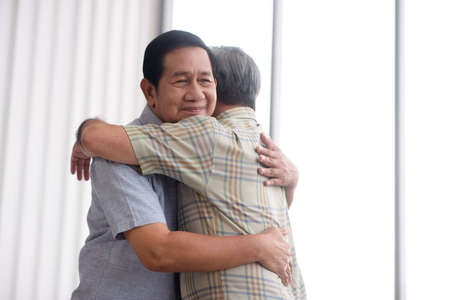 Asian grandpa hug with his friend in living roomの写真素材