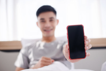 asian guy show mobilephone blank screen on the bedの写真素材