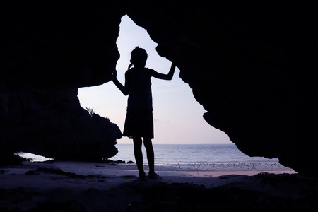 Girls stand in front of a cave on the beach at sunset.