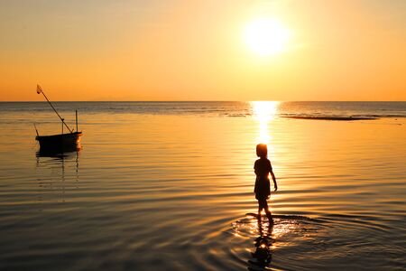 A girl walks on the beach and fishing boats at sunset.