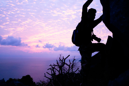Man with camera climbing up to the rock for shooting pictures of sunrise.の写真素材