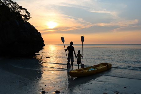 Man and daughter kayaking on the beach with sunset background.の写真素材
