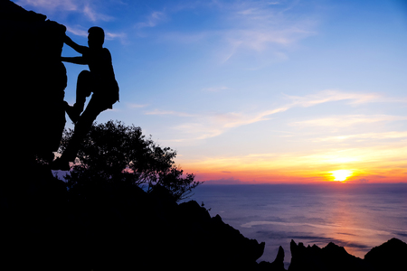 Man with camera climbing up to the rock for shooting pictures of sunsetの写真素材