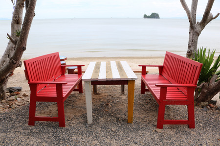 Red wooden table and chairs on the beach.