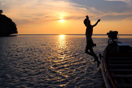 The girls jump from a long-tail boat with sunset.の写真素材