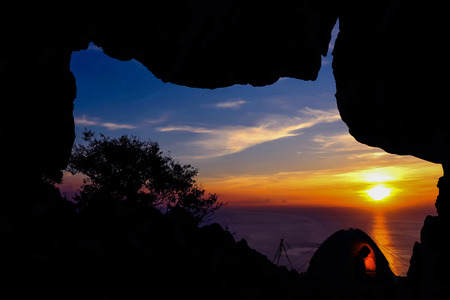 The camping in front of the cave on the mountain with the shadow of a woman in the tents at sunset.の写真素材