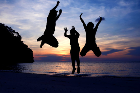 The family jumped on the beach at sunset.の写真素材