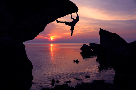 Man climbing the rocks near the sea with purple sky sunset background.の写真素材