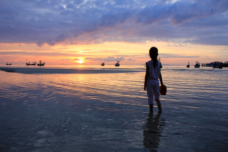 Asian girl holding shoes looking sunset on the beach.の写真素材