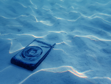 Compact camera on the sand with light reflected under the sea water.
