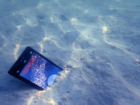 Mobile phones on the sand under the sea water.の写真素材