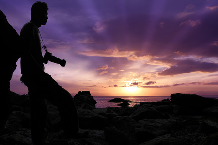 Silhouette photographer standing on the rocks by the sea with purple sky sunrise in the morning.の写真素材