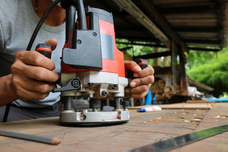 Asian workers using electric routering to cut down stripes on the wood.