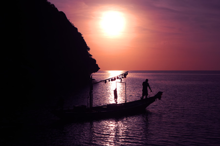 Silhouette lifestyle of fishermen with fishing boat by the sea in the evening.の写真素材