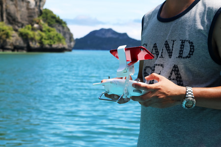 Men controlling drones camera by remote and phone on the beach near the sea.の写真素材