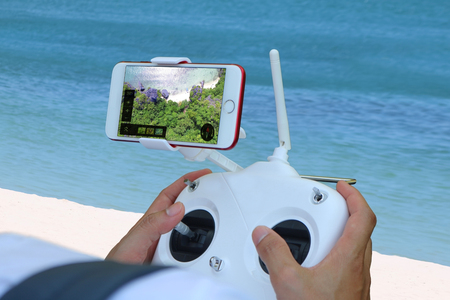 Hand controlling the drone camera by phone with view in the screen on the beach.