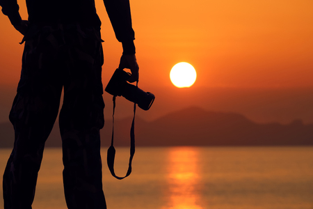 Silhouette of a photographer holding professional camera on the beach,Red sky sunrise backgroundの写真素材