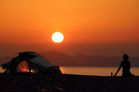Silhouette of a woman camping with tents on the beach, Red sky sunset backgroundの写真素材