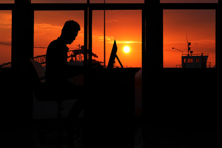 Silhouette asian business man working on a computer in the evening with sunset background.の写真素材