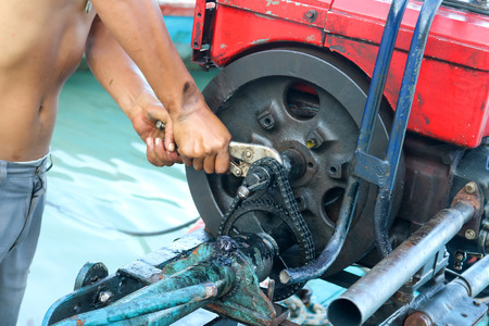 Men are repairing engines adapted for long-tail boats. Maintenance the chain gear and equipment for modified old diesel engine and spare parts in Thailand.の写真素材