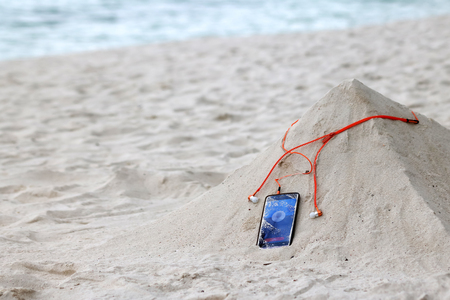 Phone and orange earphone on the sand on the beachの写真素材