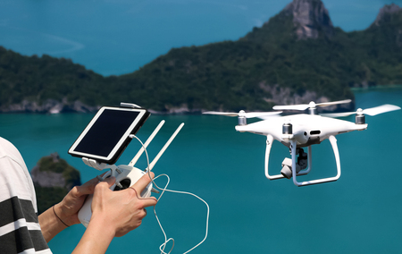 Hands holding a remote control drone camera while flying in the sky with ocean and island views...