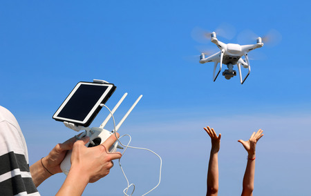 Hands holding a remote control drone camera while flying in the sky with ocean and island views backgroundの写真素材