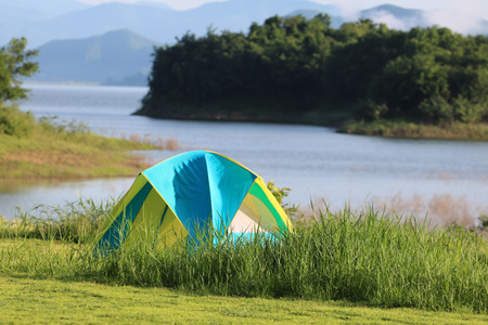 Campsite and tents on the lawn with beautiful green nature landscapes of dam water, forests, and mountains in Thailandの写真素材