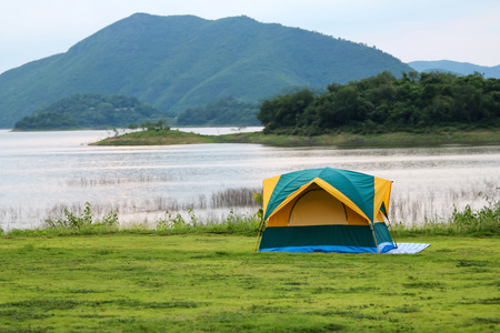 Campsite and tents on the lawn with beautiful green nature landscapes of dam water, forests, and mountains in Thailand.の写真素材