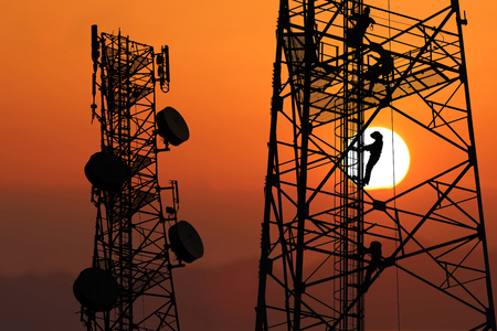 Workers are climbing to repair the telecommunication tower or poles, in the evening,Red sky sunset backgroundの写真素材
