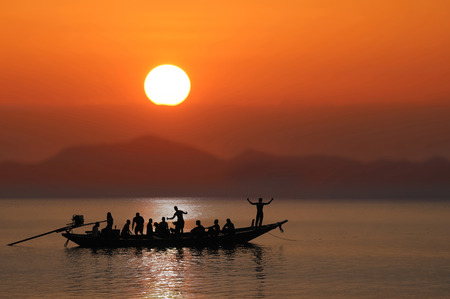 Silhouettes of people having fun on a long tail boat in the sea with sunset sky background.の写真素材
