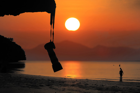 Silhouette of Camera hanging on the rocks along the beach with red sky sunset background.の写真素材