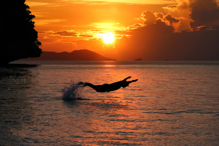 Silhouette of Man jumping or playing in the sea  with red sky sunset background.の写真素材