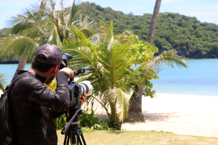 Photographer or videographer holding the video camera on a tripod on the beachの写真素材