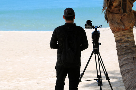 Photographer or videographer holding the video camera on a tripod on the beach