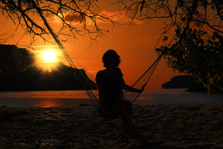 Woman lying on a hammock by the beach at sunset and red sky background.の写真素材