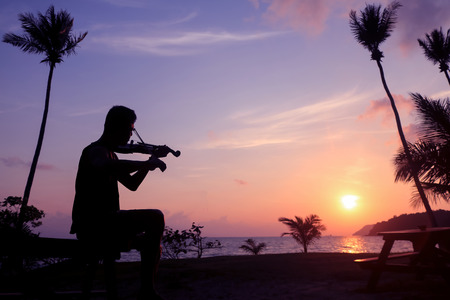 Local musicians, Asian man playing violin on the coconut beach at sunrise , Silhouette artist on purple sky background.の写真素材