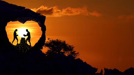 Couple on the broken heart shape rock on the mountain with red sky sunset.Silhouette Valentine background concept.の写真素材