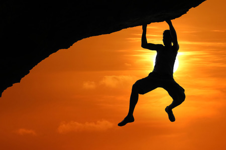 Free climbing on the mountain at red sky sunset background,Silhouette of asian man climbing rockの写真素材