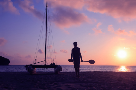 catamaran on the beach at beautiful sunrise early morning, Silhouette asian man with paddle and sailing catamaran on the beachの写真素材