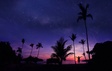 Panoramic landscape of man standing on the coconut beach with a million stars and sunrise early morning.の写真素材