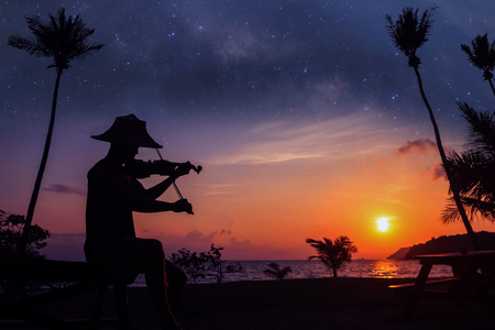 Local musicians, Asian man playing violin on the coconut beach with million stars galaxy, Silhouette artist on purple sky background.の写真素材