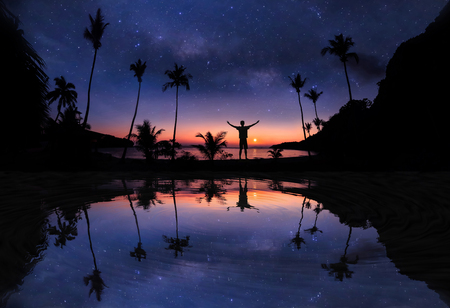 Mirror reflection of Panoramic landscape of man standing on the coconut beach with a million stars and sunrise early morning.の写真素材