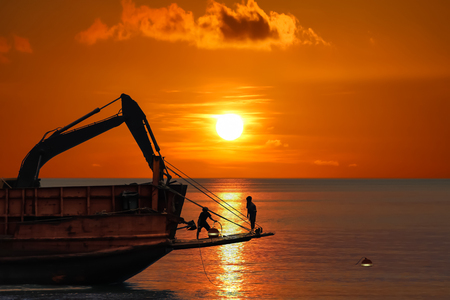 The workers are working to adjust mooring buoy on the vessel and truck excavator at sunset background.の写真素材